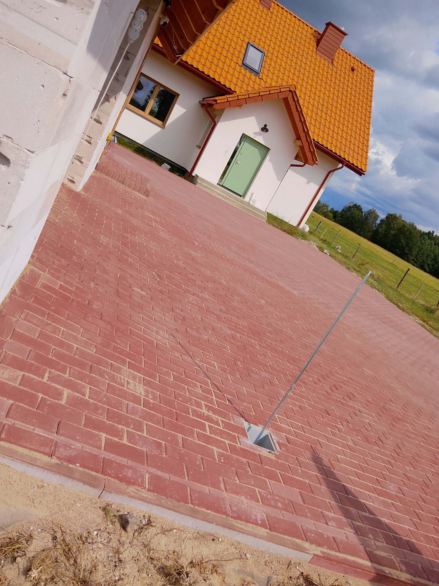 Czerwona kostka brukowa na podjeździe w Drążdżewie-Kujawach, z widocznym fragmentem domu z pomarańczowym dachem i zielonymi drzwiami. Widok z boku.