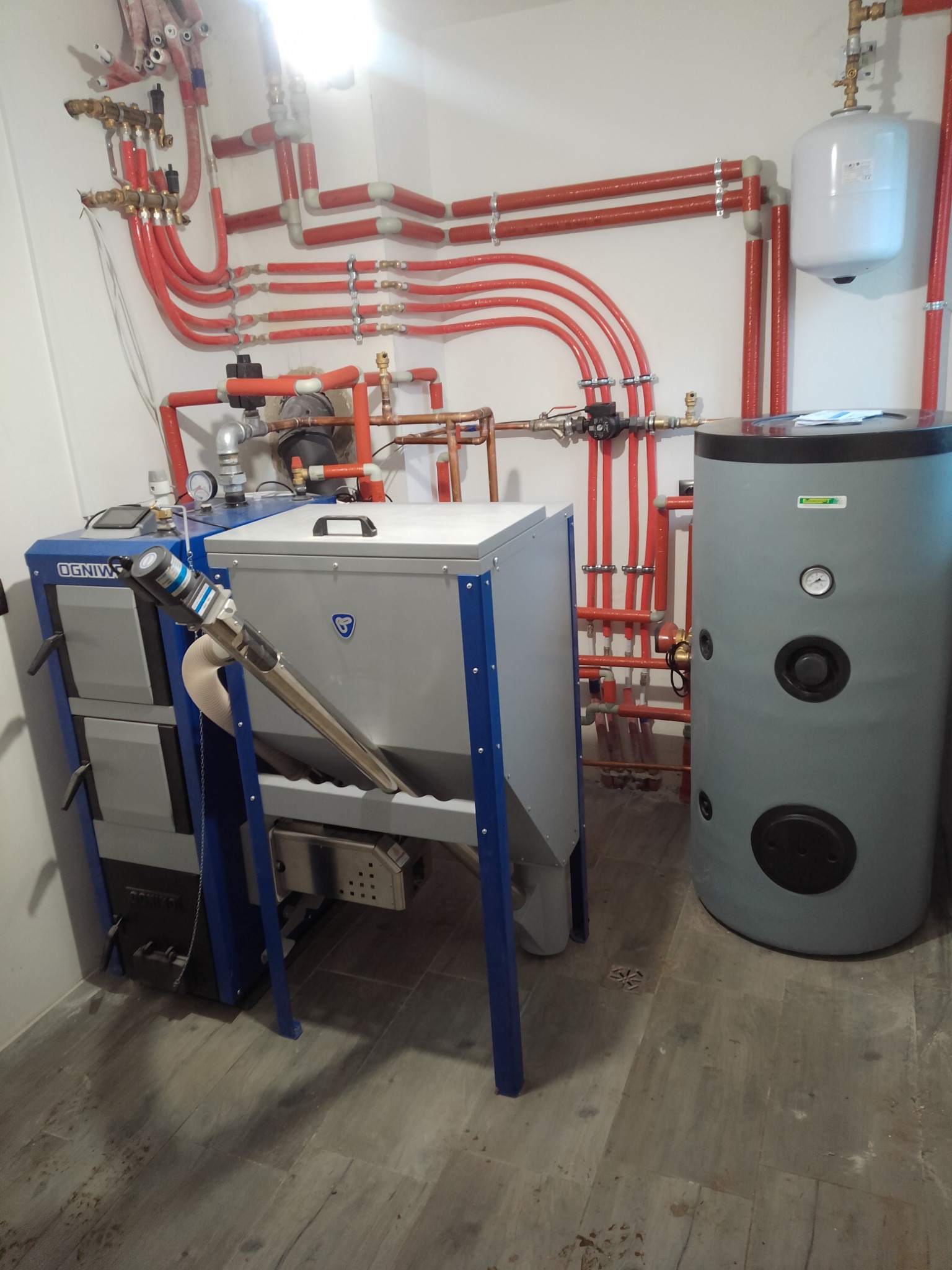 Nowoczesna kotłownia z piecem na paliwo stałe Ogniwko, zasobnikiem ciepłej wody użytkowej i rozbudowaną instalacją centralnego ogrzewania z rur w izolacji, zamontowana w pomieszczeniu wykończonym...