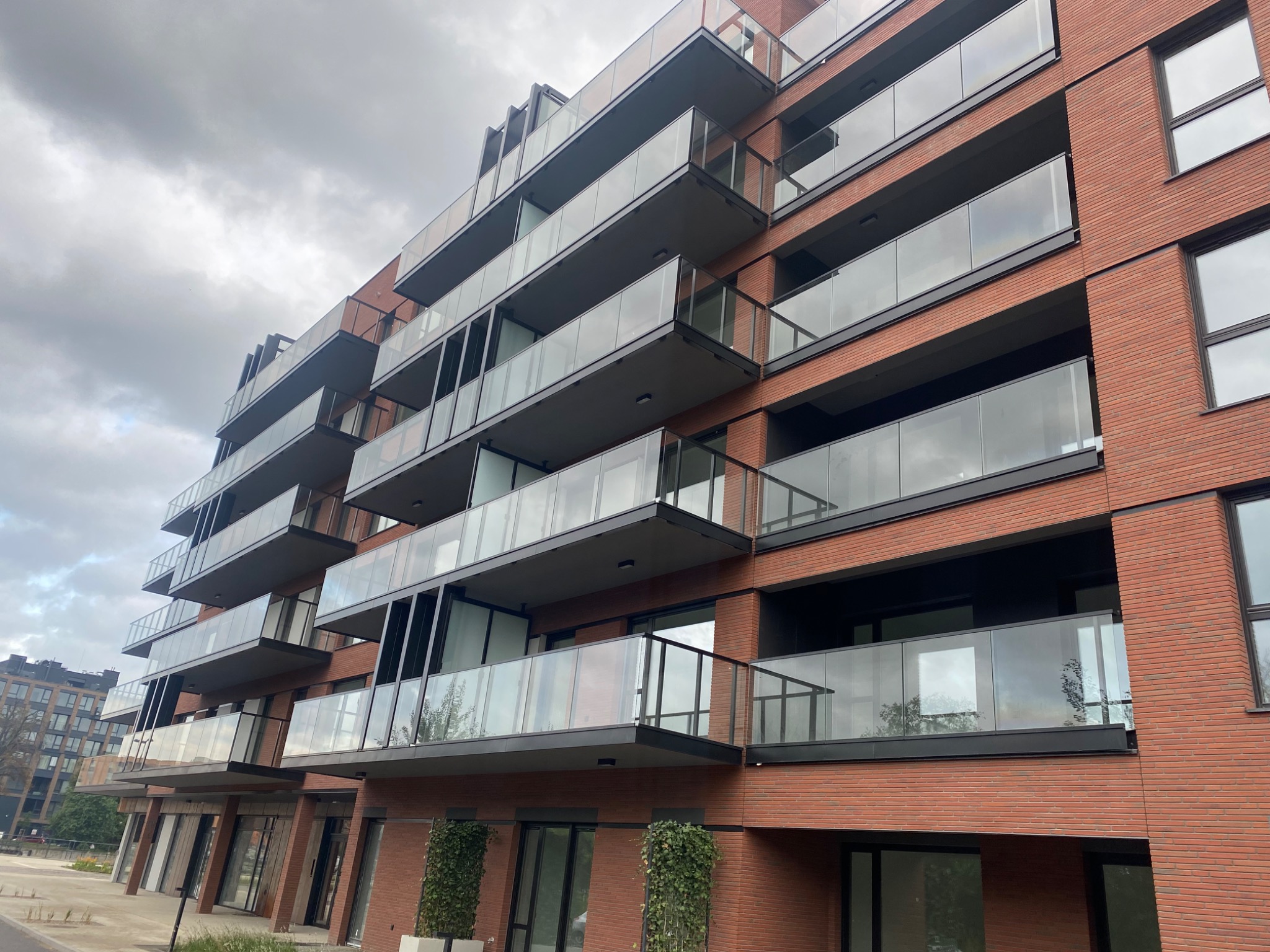Nowoczesny budynek wielorodzinny z cegły klinkierowej z balkonami z szklanymi balustradami, widok z dołu na pochmurne niebo.