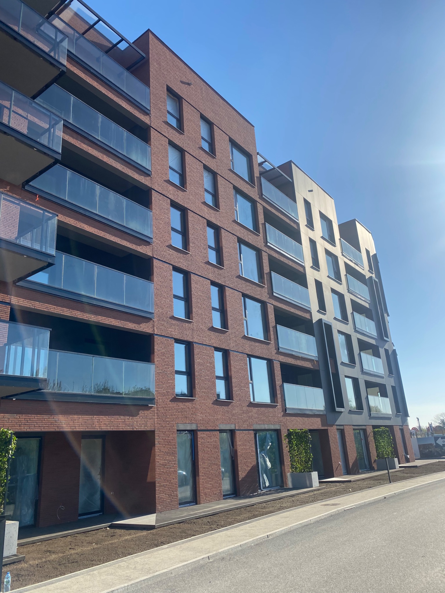 Nowoczesny budynek wielorodzinny z elewacją z elastycznej płytki klinkierowej w kolorze cegły, z balkonami z szklanymi balustradami, sfotografowany w słoneczny dzień.