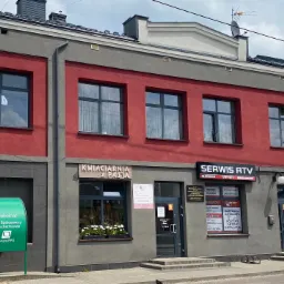 Fasada budynku z szyldem 'Serwis RTV' oferującego naprawy telewizorów, komputerów, anten i routerów, widoczna antena na dachu.