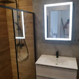 Nowoczesna łazienka z kabiną prysznicową typu walk-in z czarnymi profilami, umywalką z szafką w kolorze białym i podświetlanym lustrem LED, widok z boku.