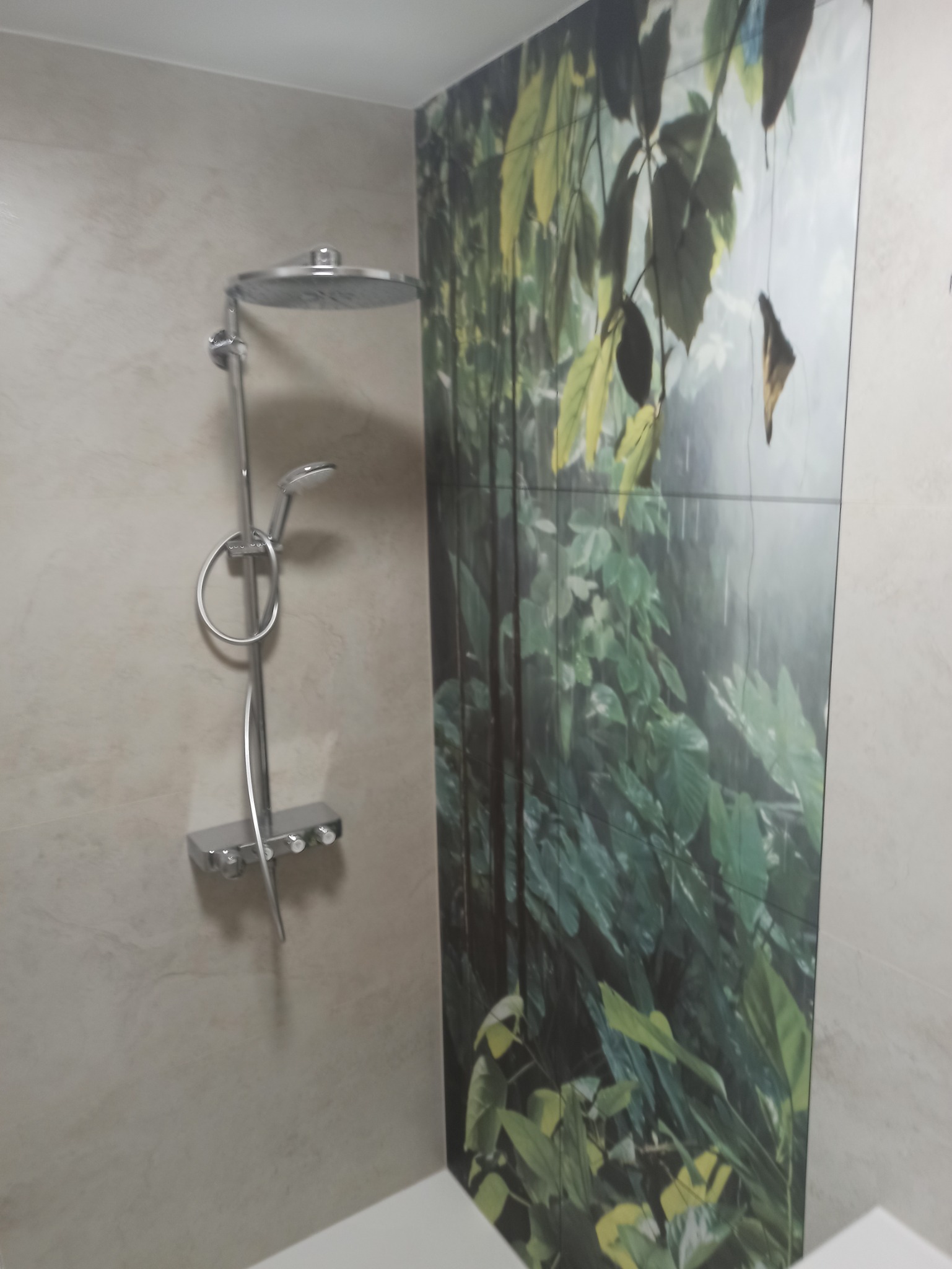 Wykończona łazienka z kabiną prysznicową i panelami ściennymi z motywem roślinnym. Nowoczesna armatura, beżowe płytki. Widok na fragment kabiny.