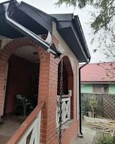 Zamontowany system rynnowy w kolorze grafitowym, widoczny z boku domu z ceglaną elewacją i łukowatym wejściem, z łańcuchem rynnowym odprowadzającym wodę.