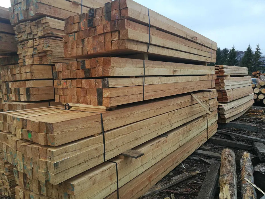 Stosy świeżo przetartego drewna budowlanego, zabezpieczone czarną taśmą, ułożone na placu składowym, widoczne ślady obróbki i naturalne sęki.