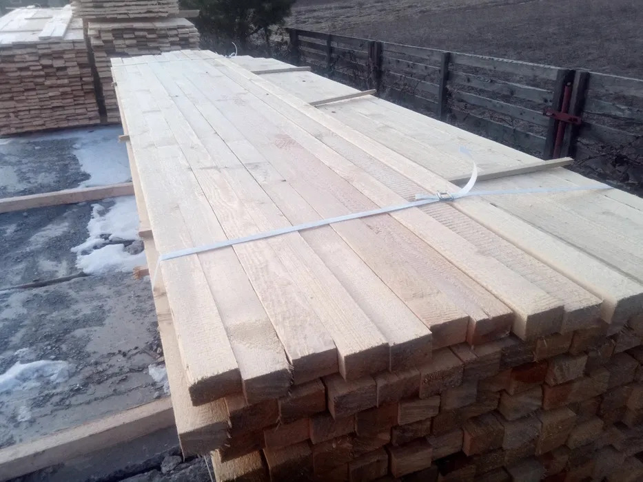 Stosy świeżo przetartego drewna budowlanego, zabezpieczone białą taśmą, składowane na zewnątrz w pochmurny dzień.