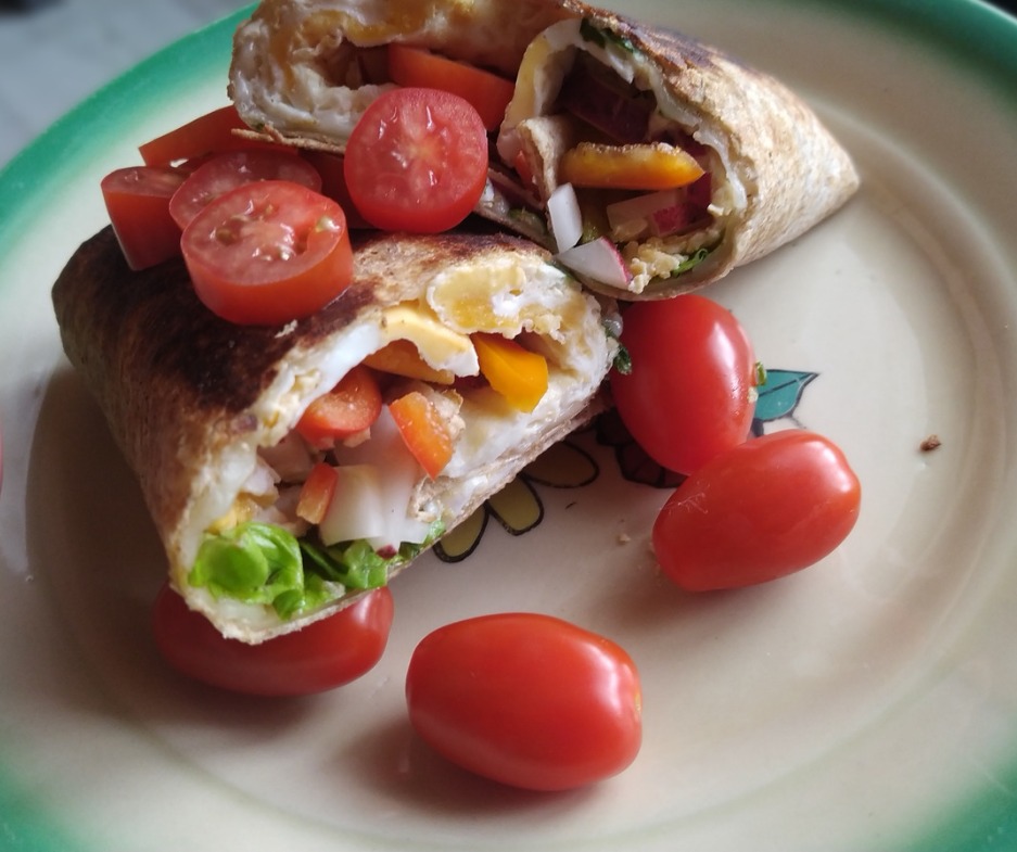 Dwa przekrojone tortille z jajkiem, warzywami i pomidorkami koktajlowymi, ułożone na talerzu z zielonym obramowaniem.