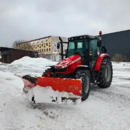 Czerwony traktor Massey Ferguson 5430 z pługiem odśnieżnym stoi na ośnieżonym placu, w tle budynki i pochmurne niebo.
