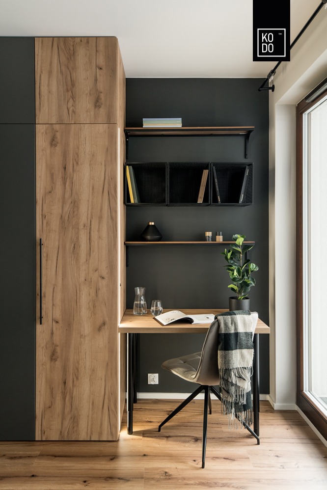 Nowoczesny kącik do pracy z biurkiem z jasnego drewna, krzesłem obrotowym, szafą z oświetleniem LED i półkami na tle ściany w kolorze grafitowym.