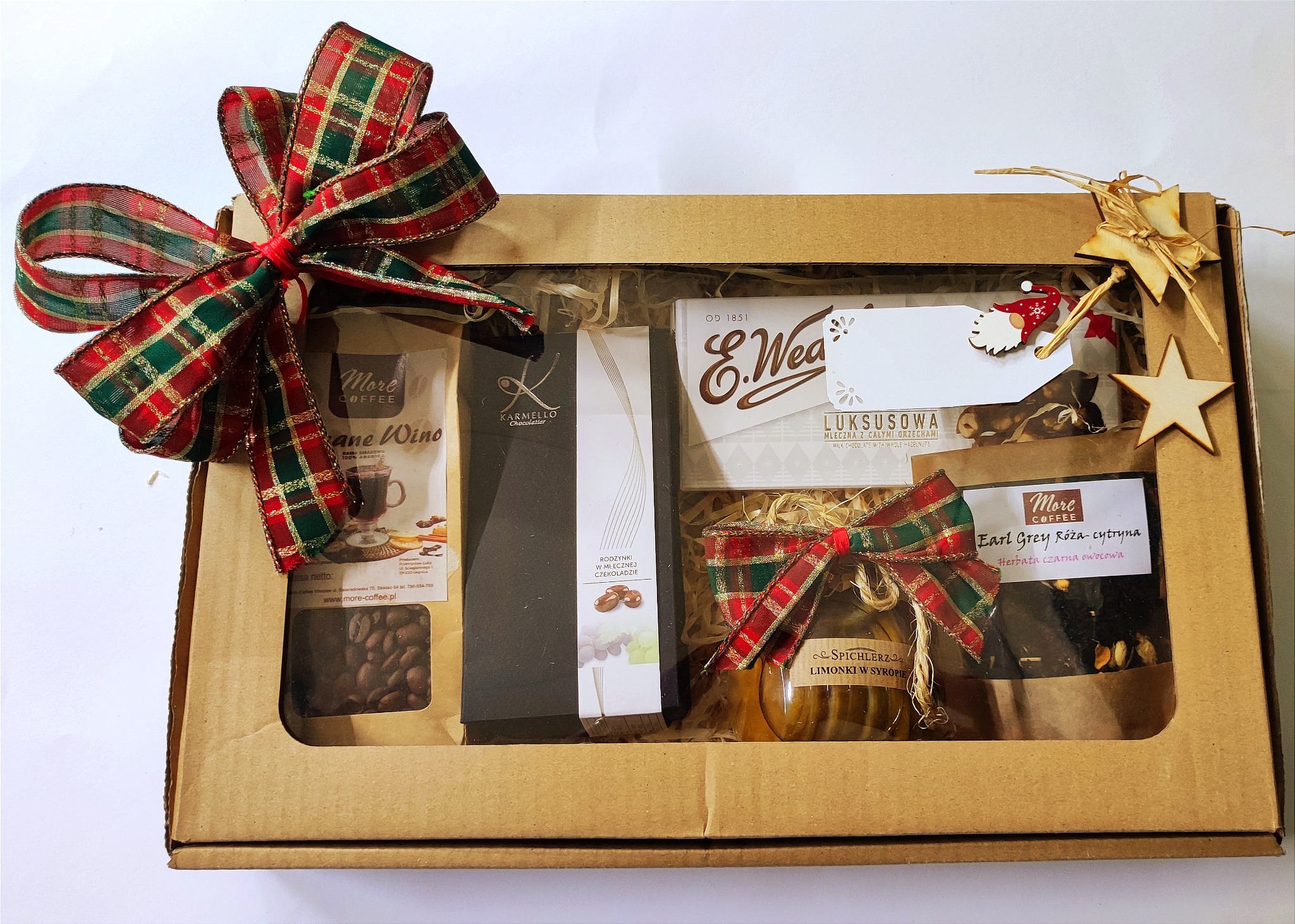 Kartonowe pudełko z prezentami, zawierające kawę ziarnistą, czekoladę, herbatę Earl Grey i limonki w syropie, ozdobione świątecznymi kokardami w kratę i drewnianymi gwiazdkami.