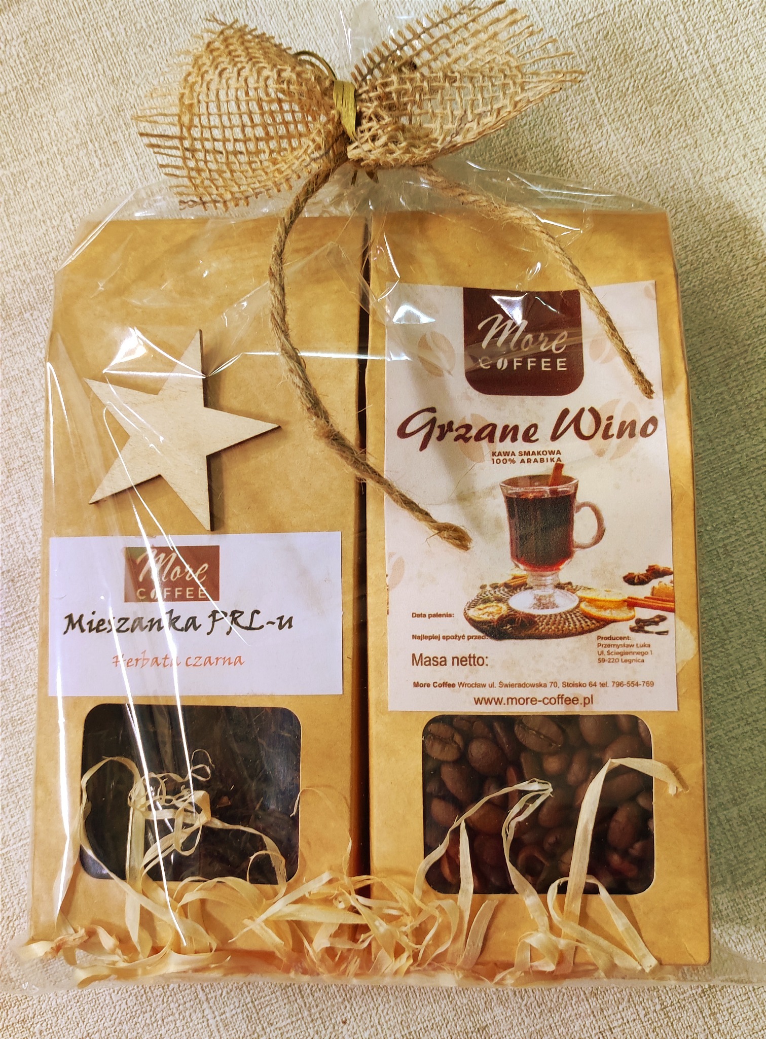 Zestaw prezentowy z kawą smakową 'Grzane Wino' i herbatą czarną 'Mieszanka PRL-u', zapakowany w celofan z jutowym sznurkiem i drewnianą gwiazdką.