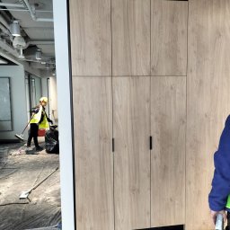 Krzysztof Lubieniecki - Montaż szafy wnękowej z drewnopodobnymi frontami w biurze w Warcie Bolesławieckiej, widoczna osoba sprzątająca po instalacji.