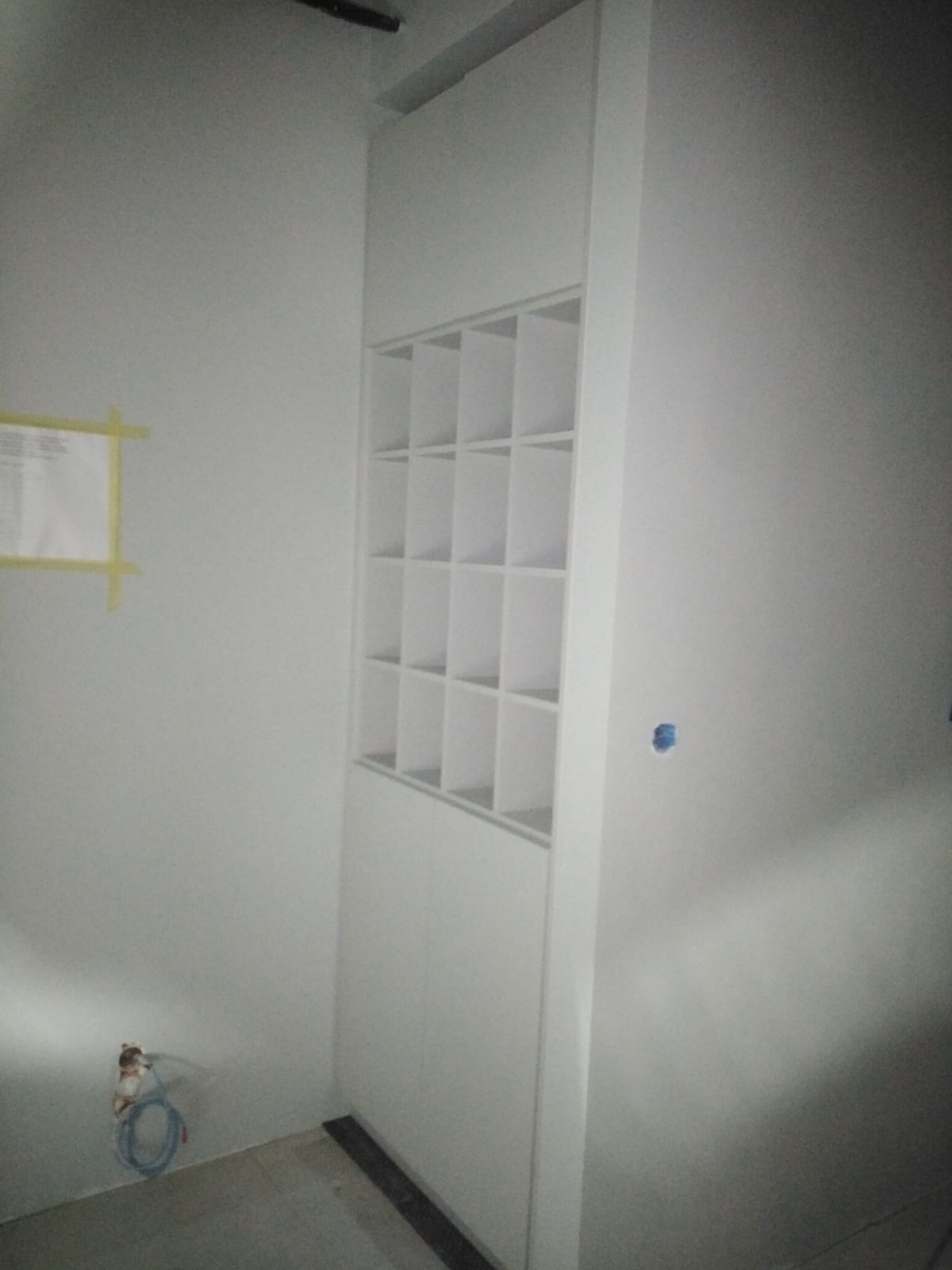 Biała szafa wnękowa z otwartymi półkami w górnej części, widoczne przewody wystające ze ściany, przygotowana do dalszego wykończenia.