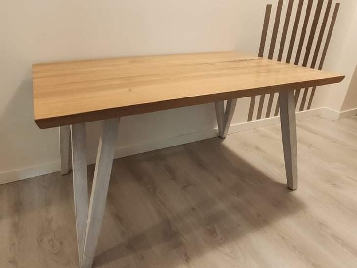 Blat drewniany z jasnego drewna na białych, skośnych nogach, wykonany w Witkowo drugie, na tle ściany z dekoracyjnymi paskami.