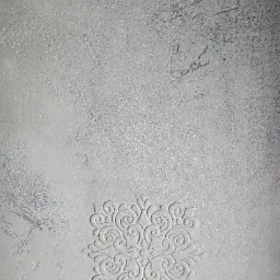 Szara ściana z dekoracyjnymi tynkami strukturalnymi i wytłoczonymi wzorami roślinnymi.