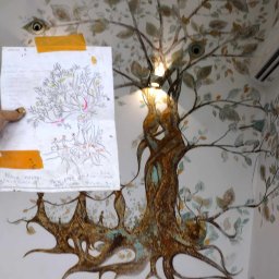 Marta Karpisz - tynkowanie dekoracyjne - Ręcznie malowane drzewo na ścianie, z widoczną lampą w koronie i szkicem koncepcyjnym przyklejonym taśmą, przedstawiającym podobny motyw.
