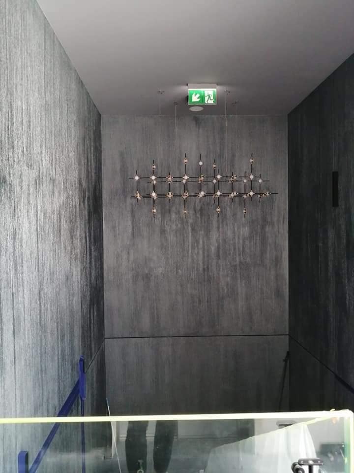 Korytarz z dekoracyjną, nowoczesną lampą sufitową w kształcie kraty z białymi kulkami na tle ściany o fakturze imitującej deszcz.