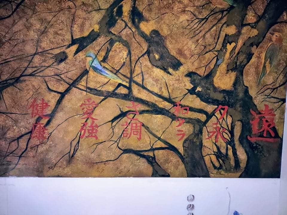 Tekstura ściany imitująca malowidło z motywem drzewa, ptaków i czerwonych znaków orientalnych.