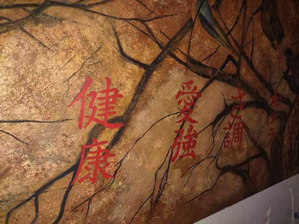 Tekstura ściany z brązowo-złotym tłem i czarnymi gałęziami, pokryta czerwonymi znakami w stylu orientalnym.