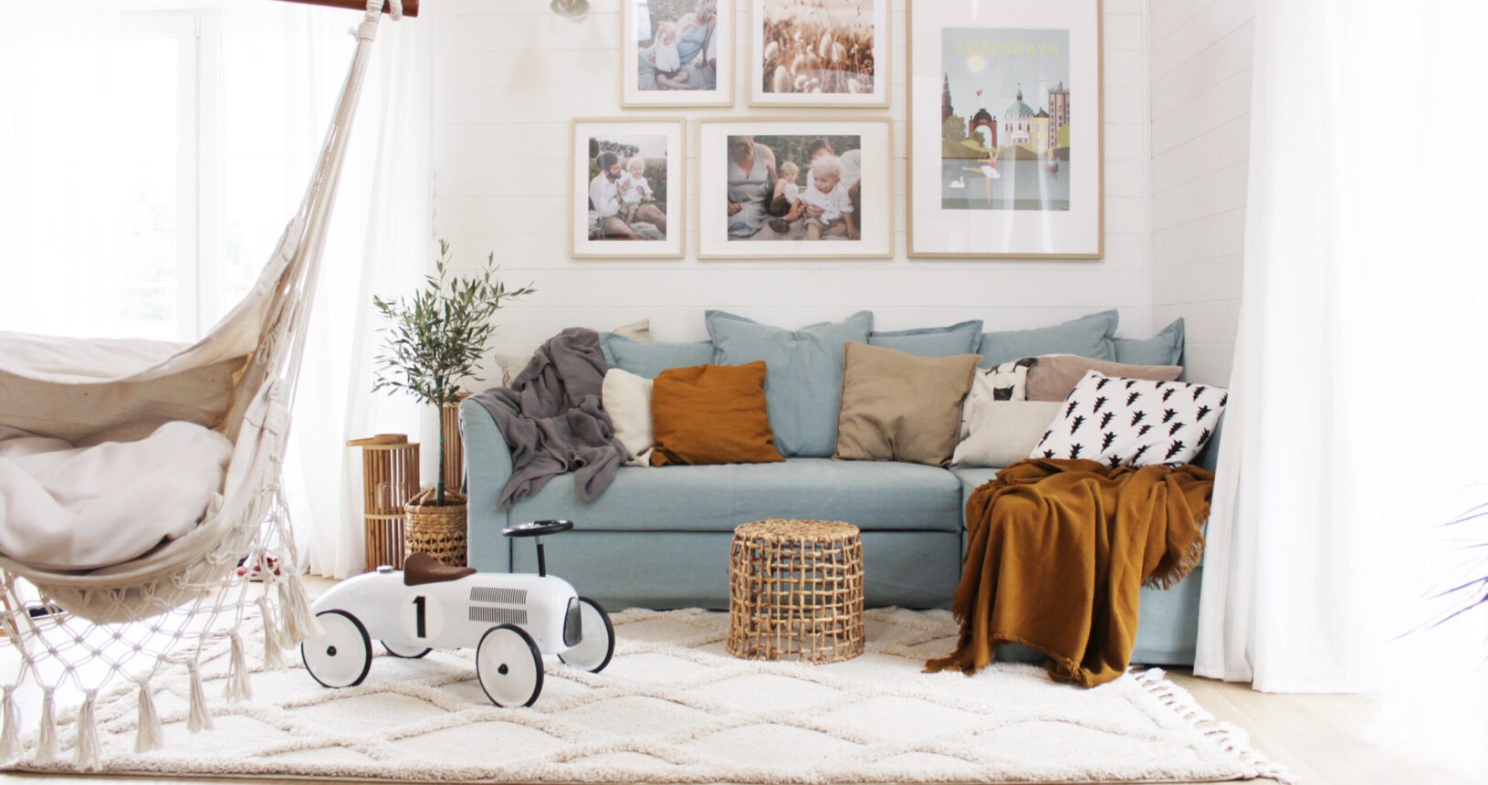 Jasny salon w stylu skandynawskim z błękitną sofą, wiszącym hamakiem z frędzlami, dywanem w romby i dekoracjami ściennymi w ramkach.