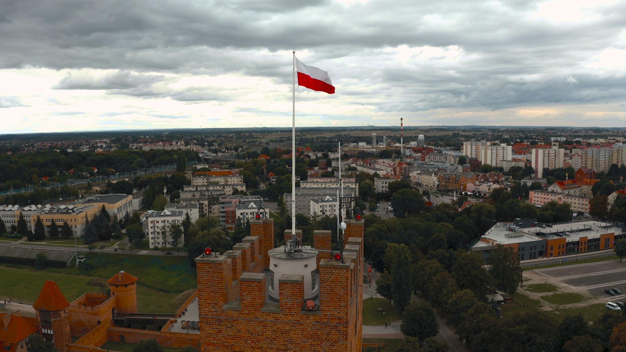 Panorama miasta z lotu ptaka, z widocznym zamkiem krzyżackim w Malborku i powiewającą polską flagą na wieży.