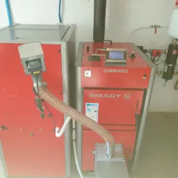 Dwa kotły grzewcze marki DEFRO, model SMART S, z widocznymi panelami sterowania i elementami instalacji, w pomieszczeniu z jasnymi ścianami i podłogą.