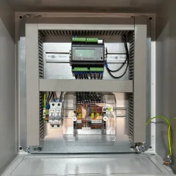 Wnętrze rozdzielnicy elektrycznej z zamontowanymi zabezpieczeniami, modułem pomiarowym Lumel NR30T i listwami zaciskowymi, widoczne przewody i elementy montażowe.