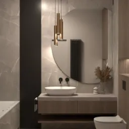 Nowoczesna łazienka z marmurowymi płytkami, okrągłym lustrem, wiszącą misą WC i umywalką nablatową, oświetlona lampą wiszącą z złotymi elementami.