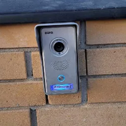 Zamontowany wideodomofon marki Eura na ceglanym słupku ogrodzeniowym, widoczny ekran z nazwą ulicy 'Zawilców 2'.