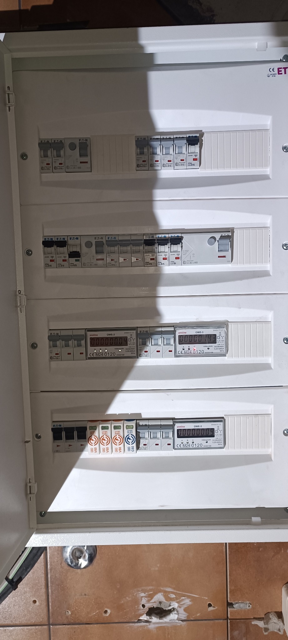 Rozdzielnica elektryczna z zamontowanymi bezpiecznikami i licznikami energii elektrycznej. Widoczne elementy marki Eaton i Onnline. Ujęcie z bliska.