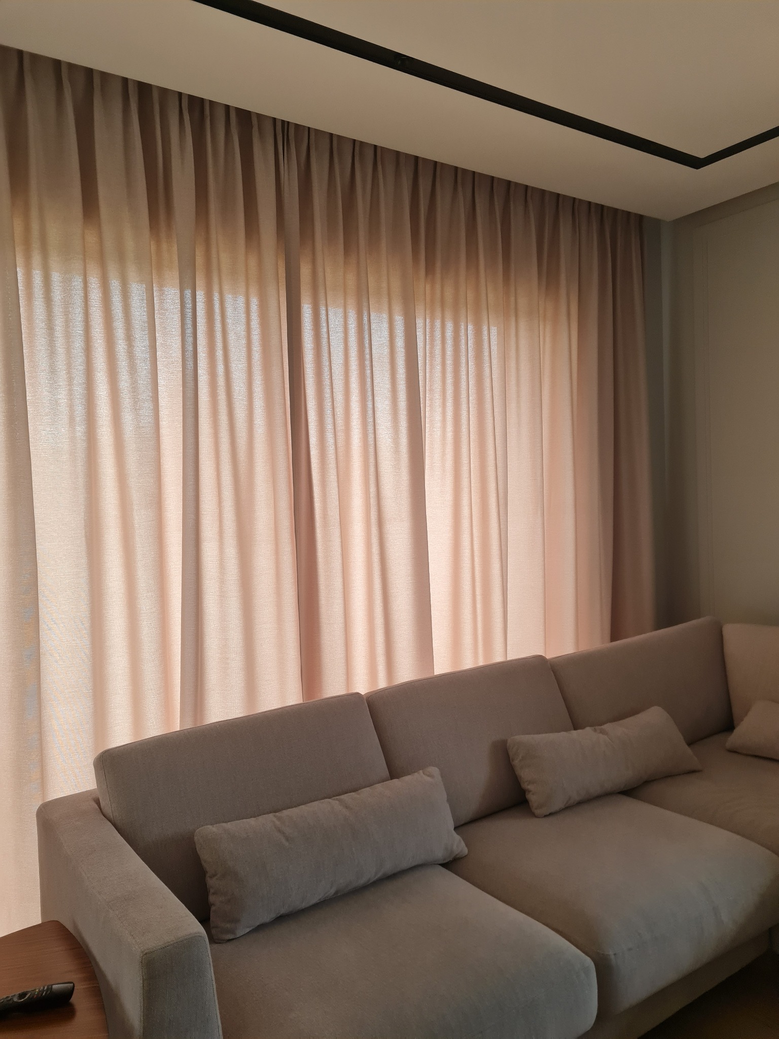 Jasne, półprzezroczyste zasłony w salonie z beżową sofą, widoczne delikatne marszczenia i wpadające światło słoneczne.