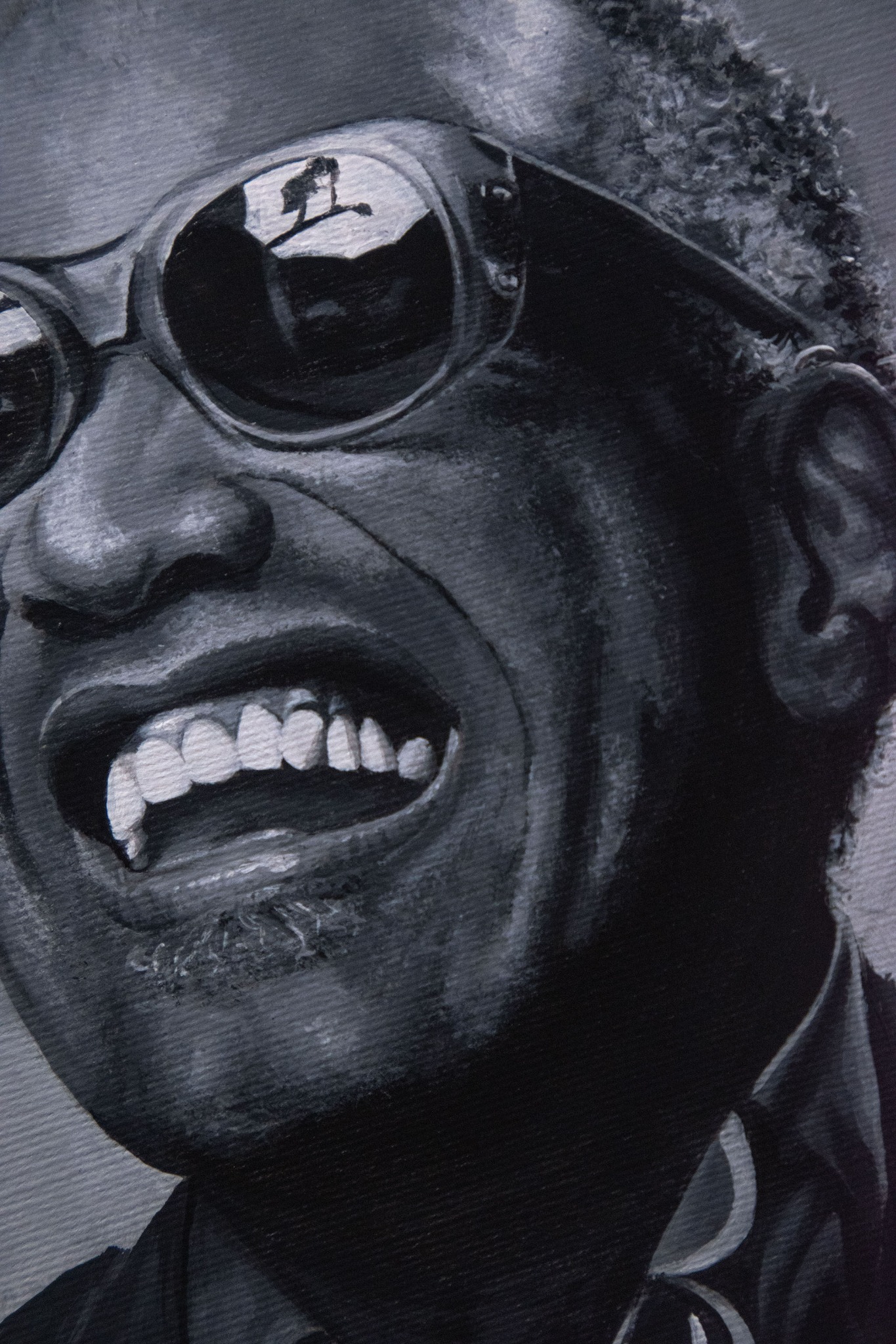 Czarno-biały portret malarski uśmiechniętego mężczyzny w okularach przeciwsłonecznych, w których odbija się sylwetka osoby stojącej na tle krajobrazu.