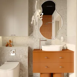 Nowoczesna łazienka z umywalką na szafce w odcieniach brązu, toaletą i szafką wiszącą. Lustro o nieregularnym kształcie z dekoracyjną lampą małpką.