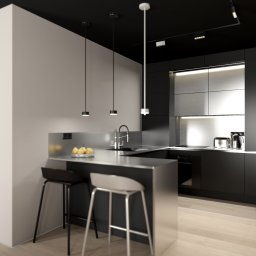 KB Interior Design Karol Budziszewski - Nowoczesna, minimalistyczna kuchnia w odcieniach szarości i czerni z wyspą i hokerami, oświetlona wiszącymi lampami. Widok na przedpokój z obuwiem.