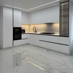 AW CENTRUM BUDOWNICTWO-REMONTY-INSTALACJE - Nowoczesna, biała kuchnia z marmurowym blatem i podłogą. Czarne akcenty w postaci armatury i uchwytów. Oświetlenie LED podkreśla minimalistyczny design.