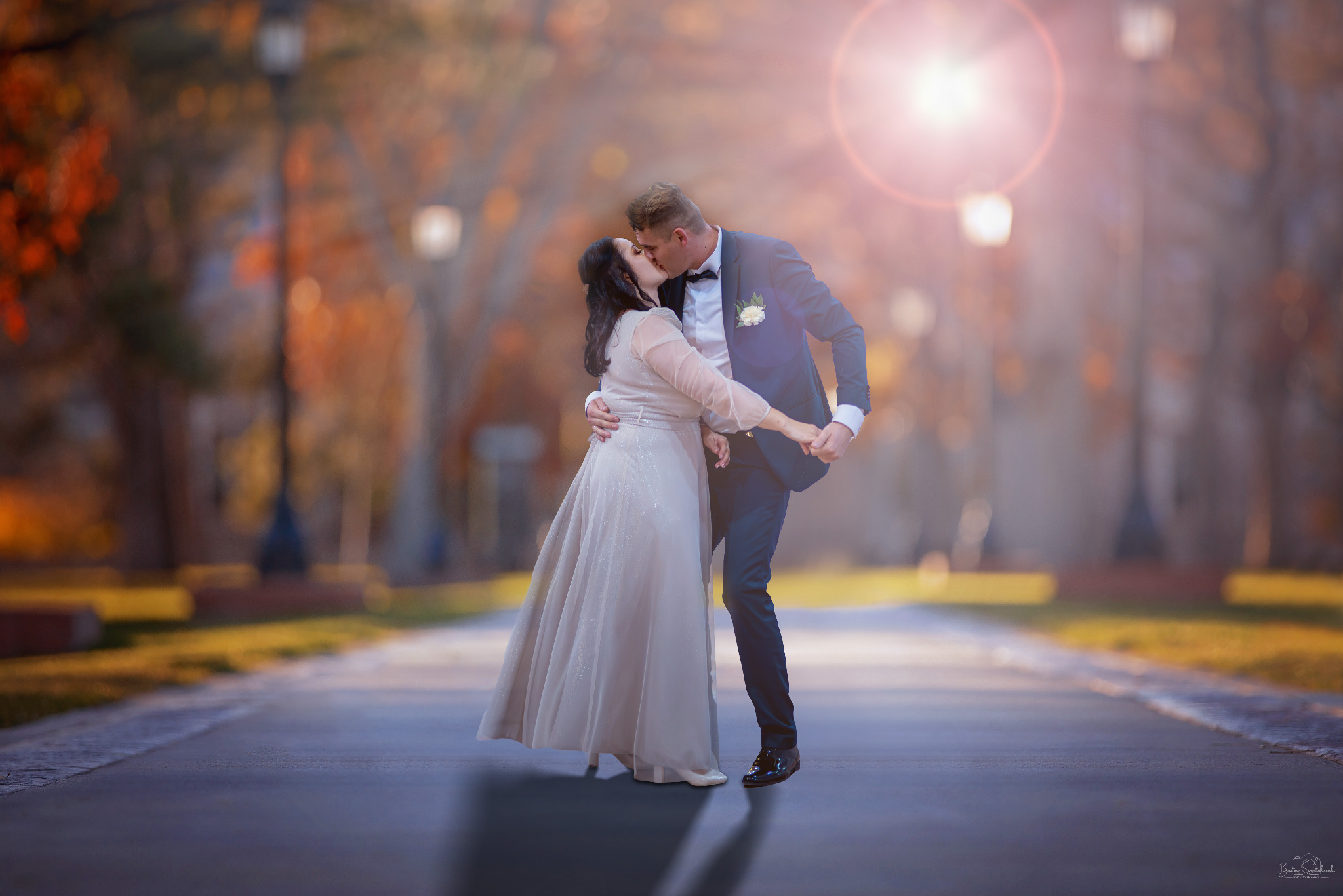 Zakochana para w eleganckich strojach całuje się na tle jesiennego parku. Ujęcie pełne ciepła i romantyzmu, z delikatnym efektem bokeh w tle.