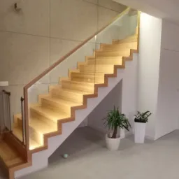 Nowoczesne schody drewniane z podświetleniem LED i szklaną balustradą w jasnym wnętrzu domu, widok na drzwi i rośliny doniczkowe.