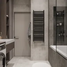 Nowoczesna łazienka w szarościach z grzejnikiem drabinkowym, wanną za szklaną ścianką i pralką obok umywalki.