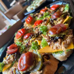 Czarny talerz z rzędami kanapek z szarpaną wieprzowiną, serem cheddar, sałatą, pomidorami cherry, piklami i sosem musztardowym, ustawionych pod kątem.