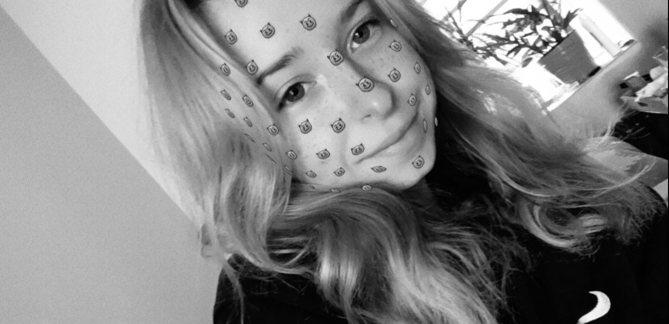 Czarno-białe selfie młodej kobiety z filtrem graficznym na twarzy, długie blond włosy, roślina w tle przy oknie.