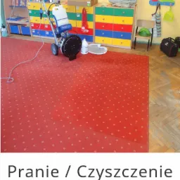 Czerwony dywan w przedszkolu czyszczony maszyną do ekstrakcyjnego prania dywanów; widoczny fragment dywanu po czyszczeniu, maszyna czyszcząca, zabawki w tle.