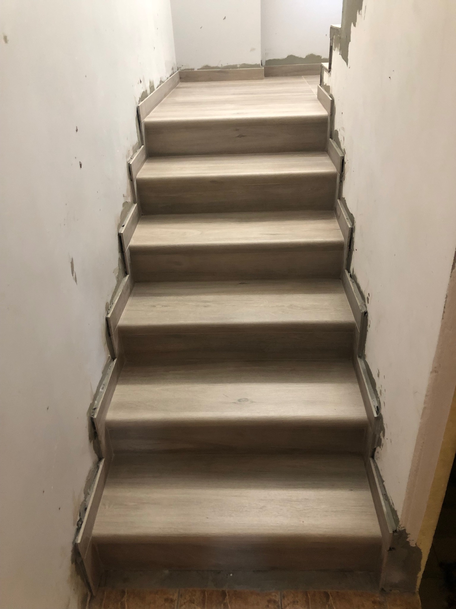 Wykończenie schodów płytkami imitującymi drewno, widoczne niedociągnięcia w postaci resztek zaprawy na ścianie.