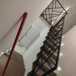 Stalmar - Nowoczesne schody z czarną, geometryczną balustradą metalową, widziane z góry. Czerwona poziomica oparta o ścianę. Oświetlenie punktowe wzdłuż schodów.