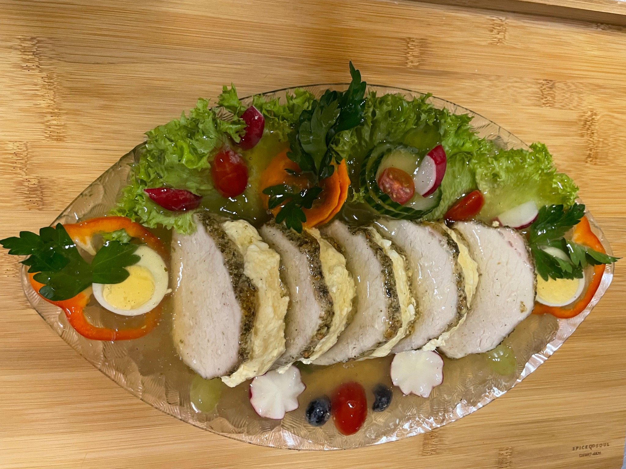 Półmisek z galaretą, plastrami mięsa, jajkiem, warzywami i dekoracjami z zieleniny na drewnianym tle.