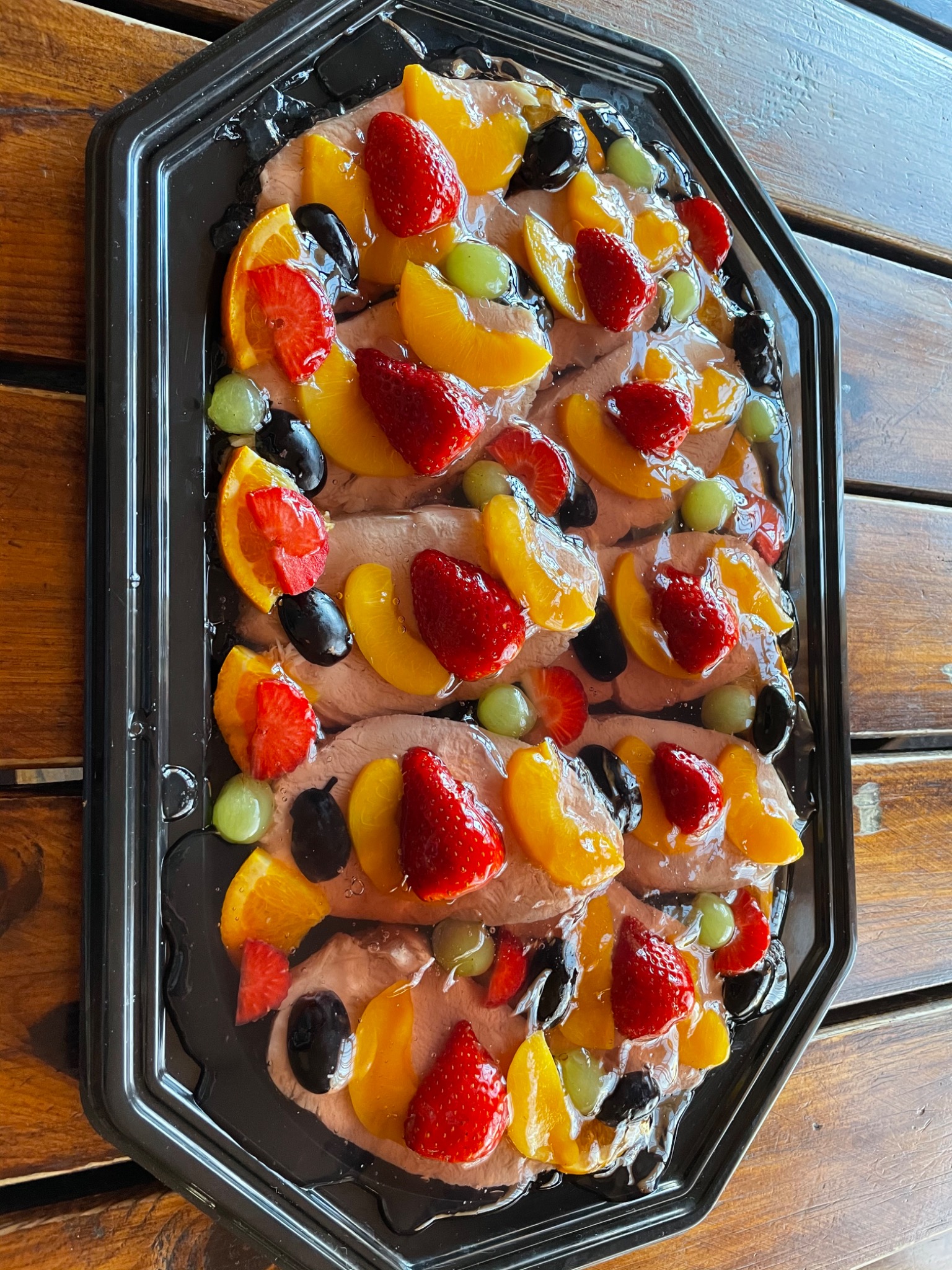 Deser z bitą śmietaną, truskawkami, brzoskwiniami, winogronami i pomarańczami ułożony na czarnej tacy na drewnianym stole.