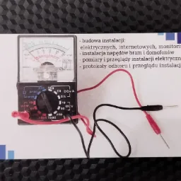 Zdjęcie wizytówki z analogowym multimetrem wskazującym napięcie, obok wypisane usługi: budowa instalacji elektrycznych, internetowych, monitoring, instalacja napędów bram i domofonów, pomiary...