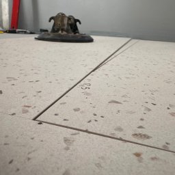 Ciężkowski Adam - Ułożone płytki podłogowe imitujące lastryko z widocznymi fugami i narzędziem do układania płytek w tle.