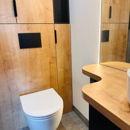 Ciężkowski Adam - Nowoczesna łazienka z podwieszaną miską WC, szafką z drewnopodobnym frontem i czarnymi akcentami, oświetlenie LED przy lustrze.