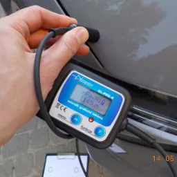 Pomiar grubości lakieru miernikiem Prodig-Tech GL-PRO-6 na szarym samochodzie, widoczny wynik 1145um, w tle kostka brukowa.