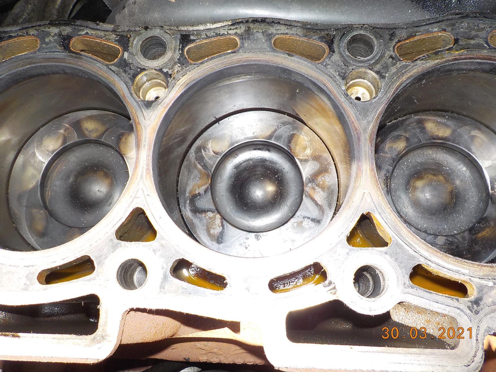 Głowica silnika samochodowego z widocznymi cylindrami i tłokami, nagar na tłokach, widoczne ślady oleju.